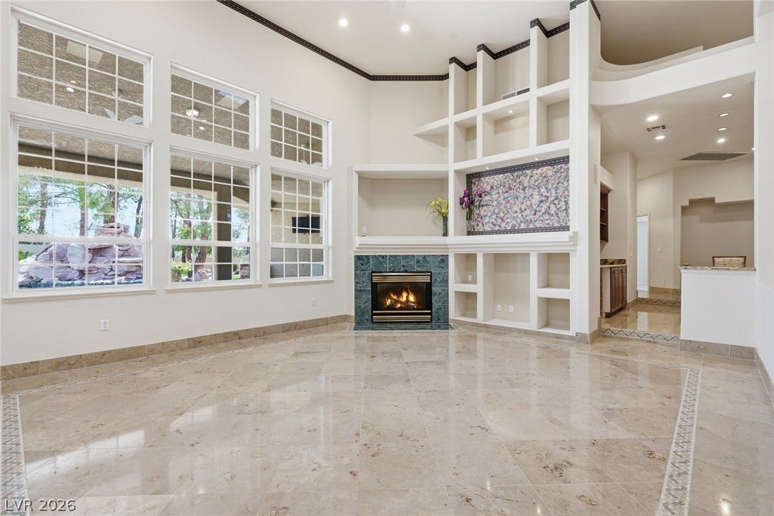2212 Chatsworth Court, Henderson, NV 89074 Floor-to-ceiling windows illuminate a spacious living area, highlighting the intricate tiled flooring and an inviting fireplace.