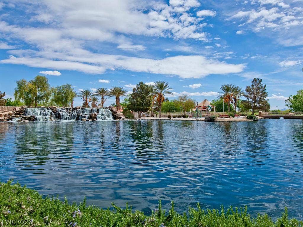 7940 Fantail Drive, North Las Vegas, NV 89084 Palm trees and a multi-tiered stone waterfall line the edge of a serene community lake.