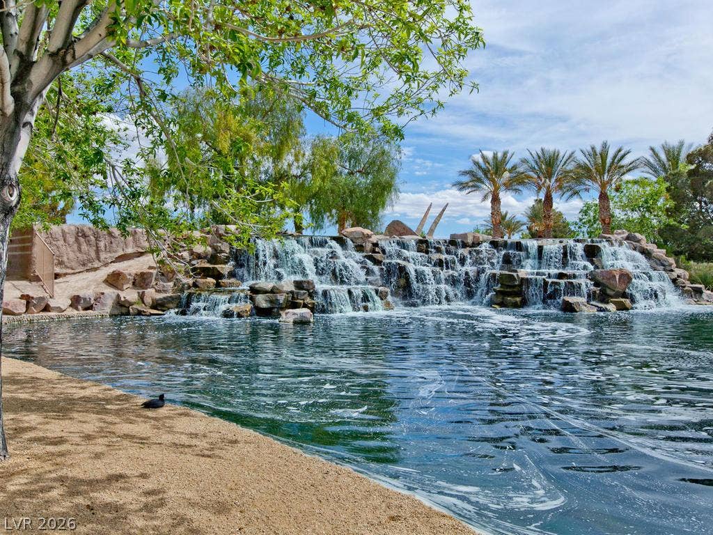 7940 Fantail Drive, North Las Vegas, NV 89084 Lush tropical palm trees and a cascading stone waterfall frame the serene community lake.