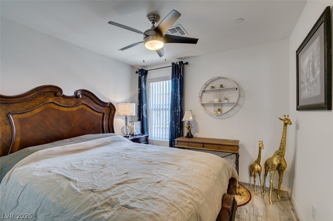 3231 Pergusa Drive, Henderson, NV 89044 A quiet bedroom features light-toned wood flooring and a large window facing the outdoors.