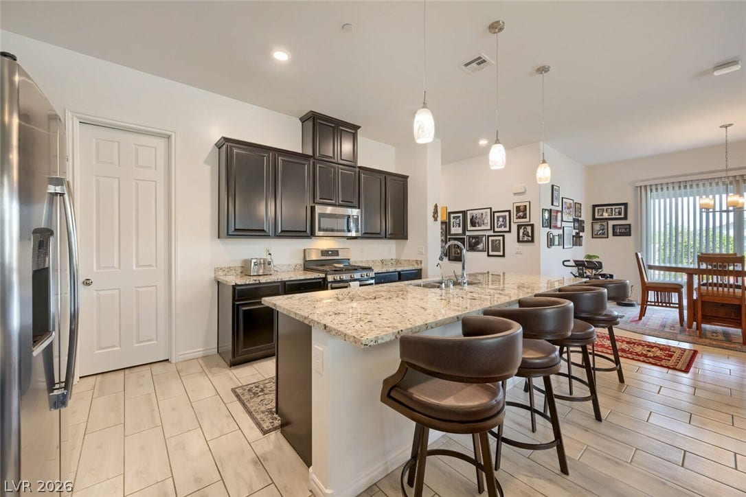 747 Orange Plume Walk, Henderson, NV 89011 Polished tile flooring flows beneath a generous stone-topped island and dark wooden cabinetry.