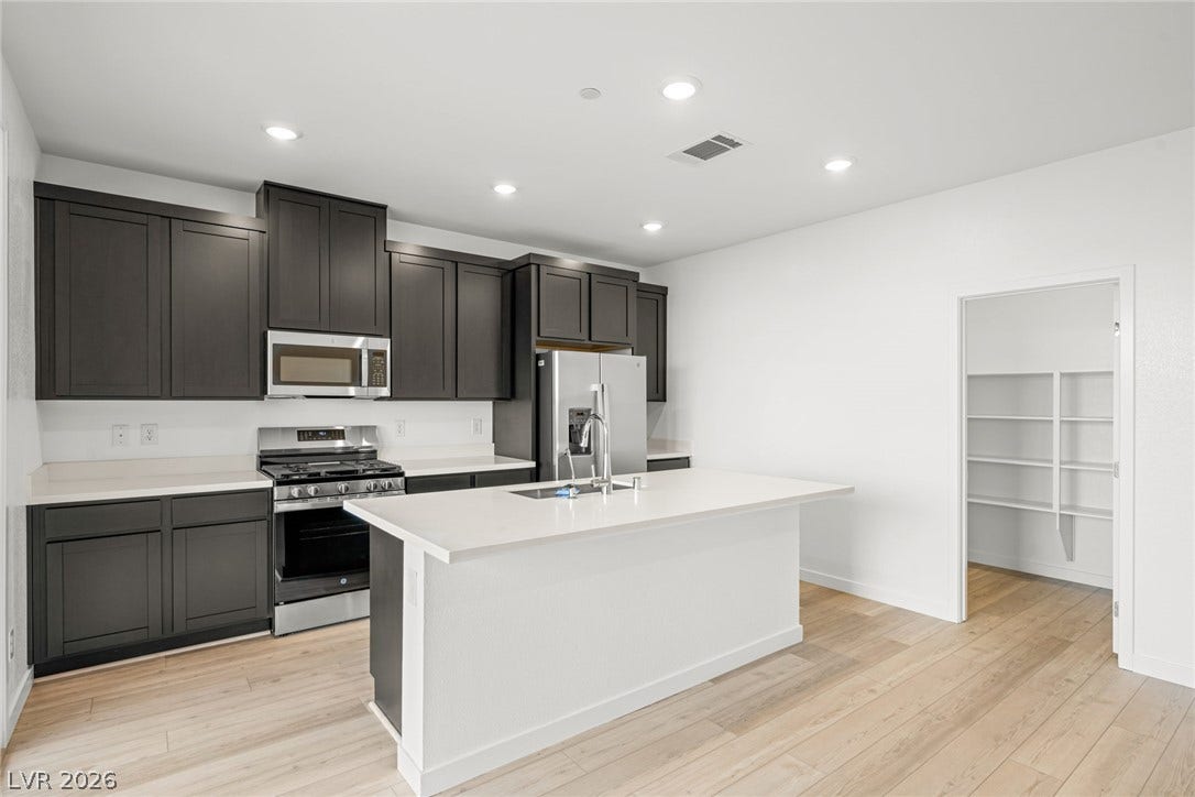 Gleaming stone countertops and dark cabinetry create a modern culinary workspace with light wood floors.
