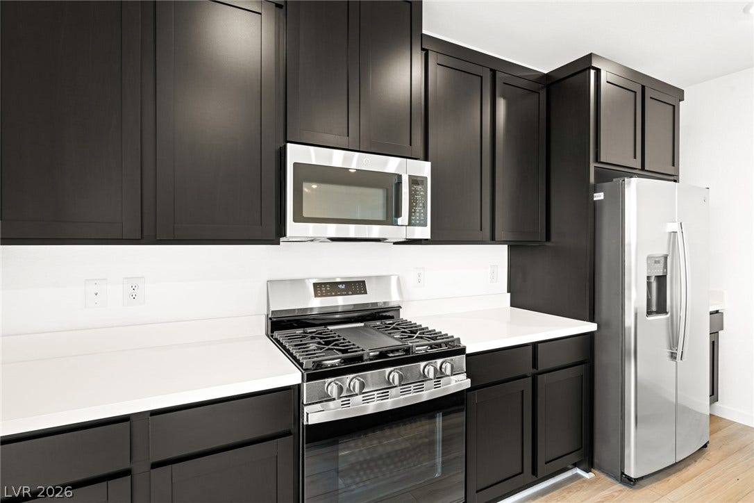 Crisp solid-surface countertops contrast with dark shaker cabinetry and modern stainless steel appliances.