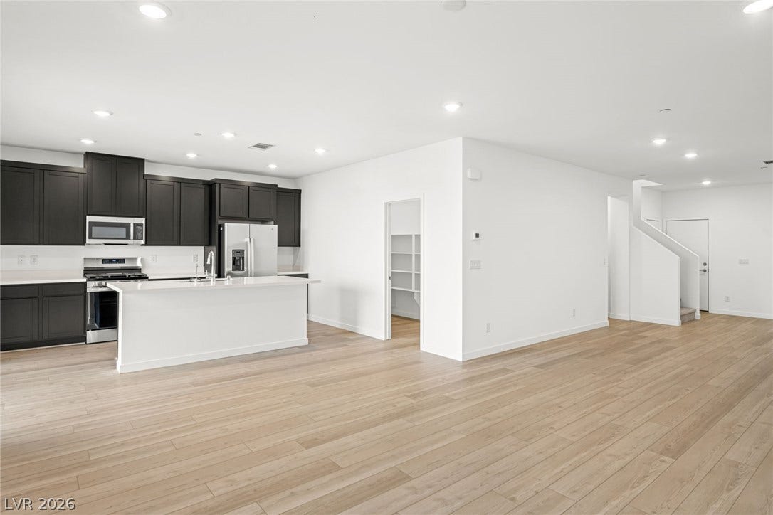 An open floorplan seamlessly connects the contemporary kitchen with light wood flooring throughout.