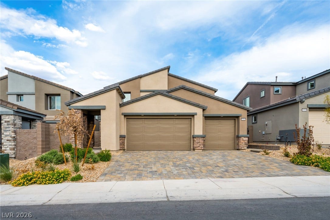 A striking modern facade with a multi-car garage, stone accents, and a paver driveway.