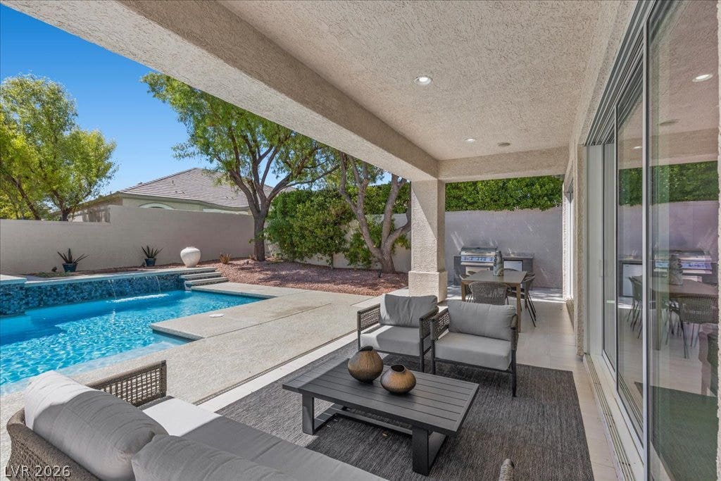 9425 Garnet Crown Avenue, Las Vegas, NV 89145 A sheltered concrete patio overlooks a sparkling blue swimming pool surrounded by mature trees.