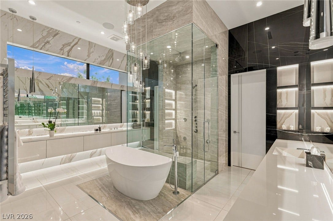 4 Chisel Crest Court, Henderson, NV 89012 Gleaming stone tiles and floor-to-ceiling glass paneling define this modern spa bathroom.