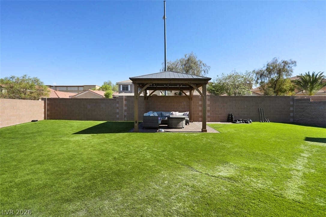 A spacious backyard with synthetic turf features a charming covered gazebo, perfect for outdoor relaxation.