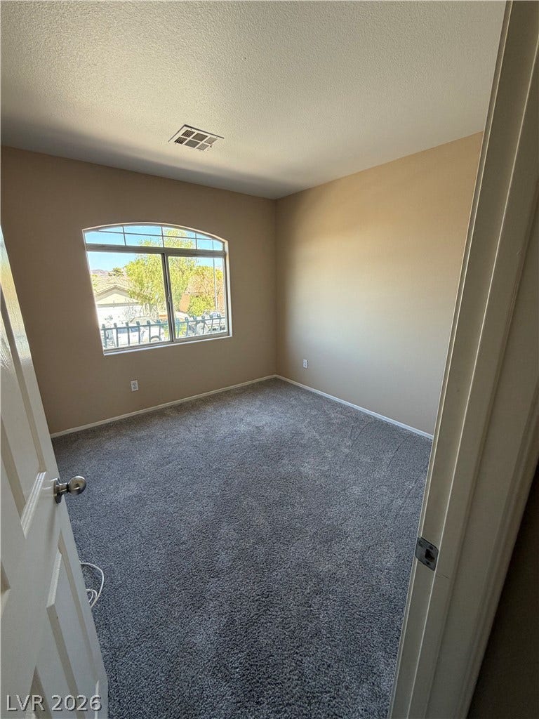 A well-lit bedroom features plush carpeting and a charming arched window with exterior views.