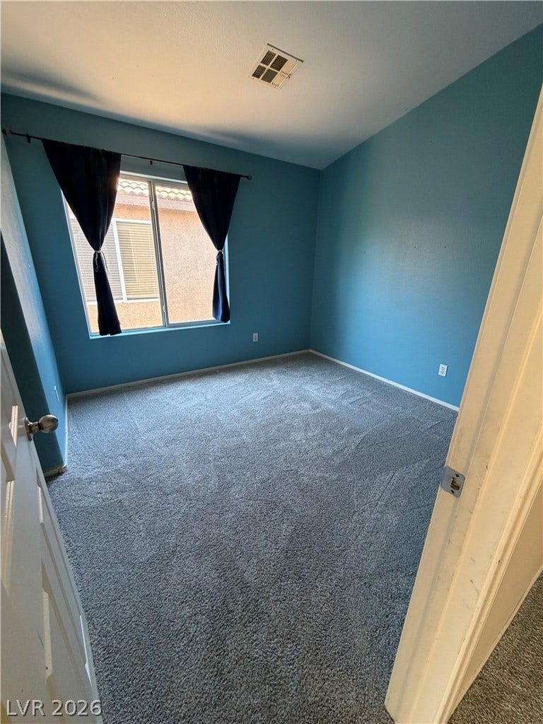 A well-lit bedroom features plush carpeting and a wide window, offering a comfortable personal space.