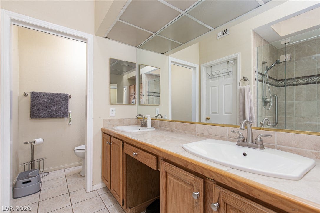 2882 Bridgepointe Drive, Las Vegas, NV 89121 Tiled flooring and a spacious double vanity with wood cabinetry anchor this classic bathroom design.