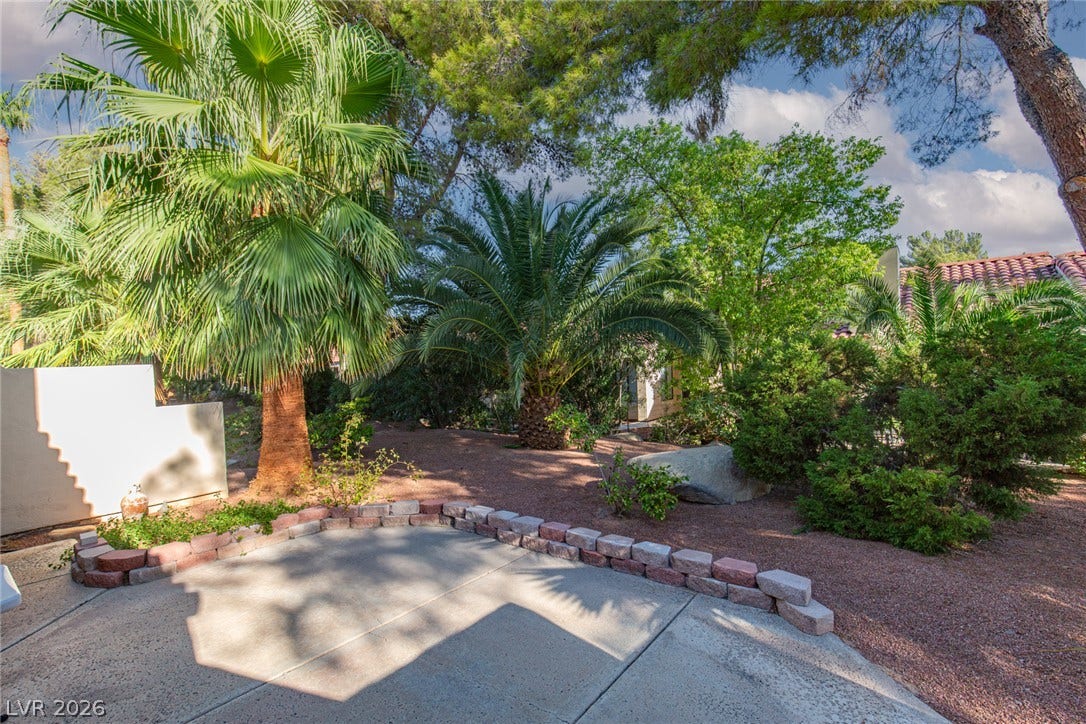 2882 Bridgepointe Drive, Las Vegas, NV 89121 Mature palms and leafy trees frame a concrete patio area bordering the gravel yard.