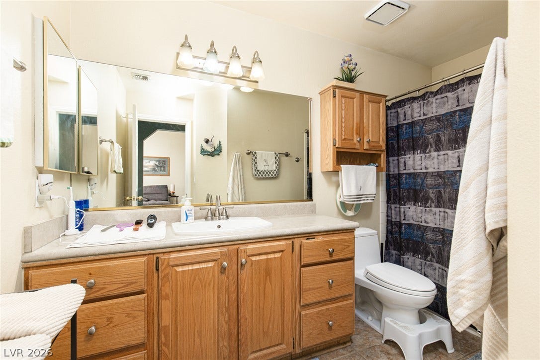 2882 Bridgepointe Drive, Las Vegas, NV 89121 Warm wood cabinetry and an expansive mirror define this functional bathroom layout.