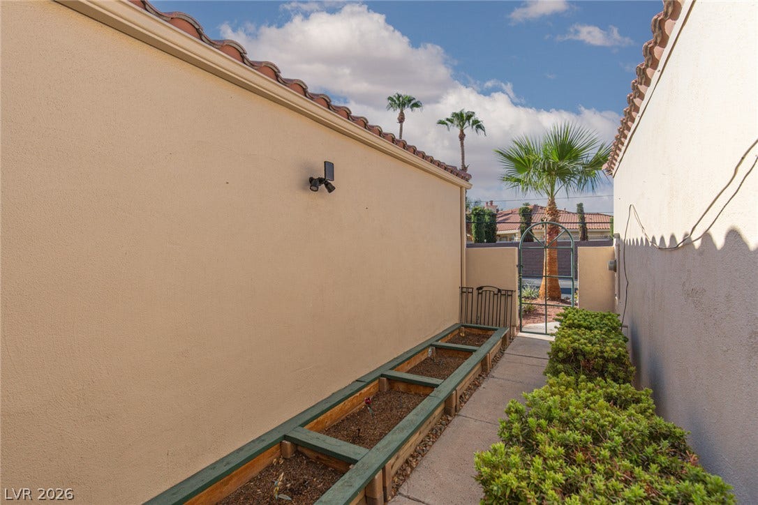 2882 Bridgepointe Drive, Las Vegas, NV 89121 A paved side pathway features built-in garden planter boxes beneath a stucco exterior and tiled roofline.