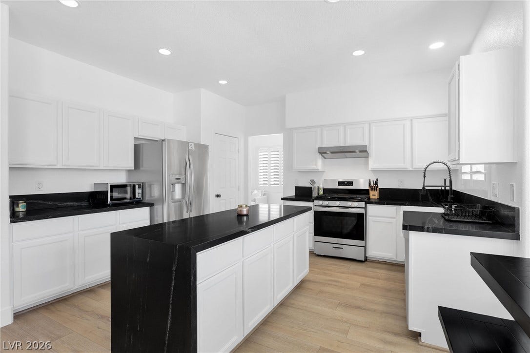 337 Teal Ridge Hills Drive, Henderson, NV 89014 Dark stone countertops contrast sharply with crisp cabinetry and light wood-plank flooring.