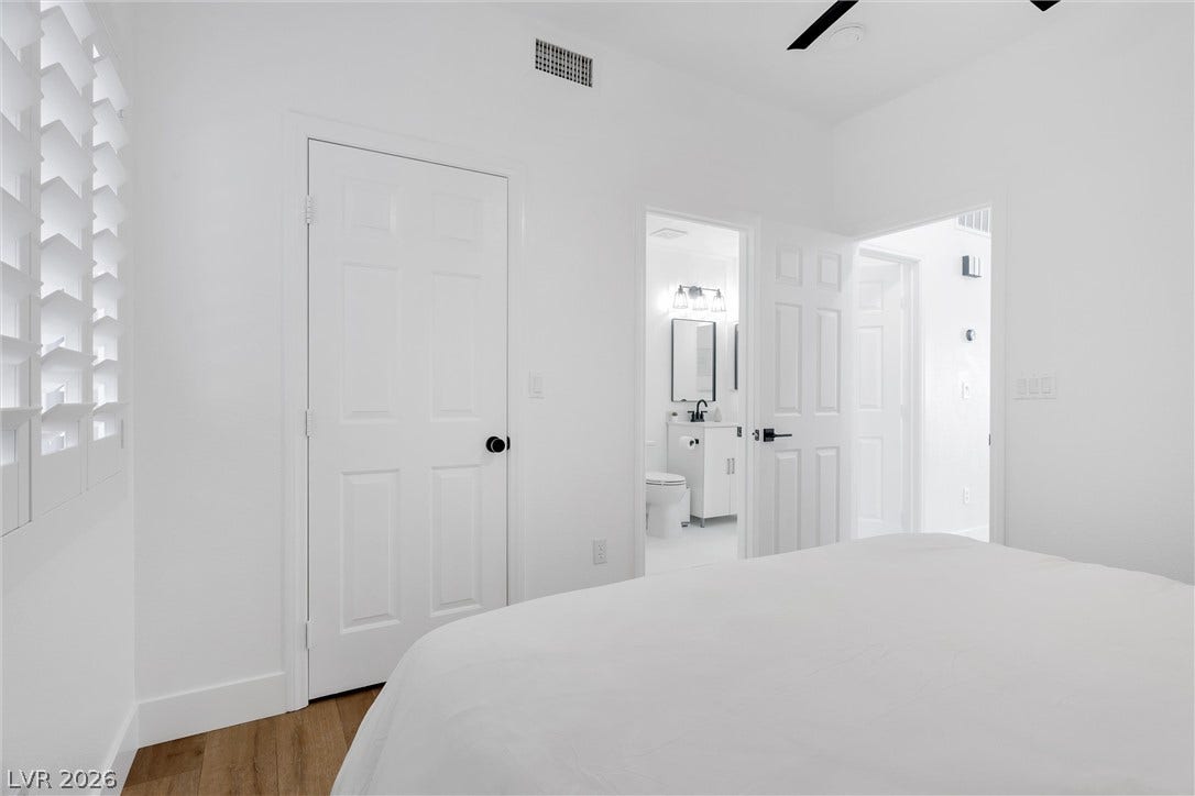 337 Teal Ridge Hills Drive, Henderson, NV 89014 Crisp white walls and warm wood flooring define this serene bedroom with ensuite access.