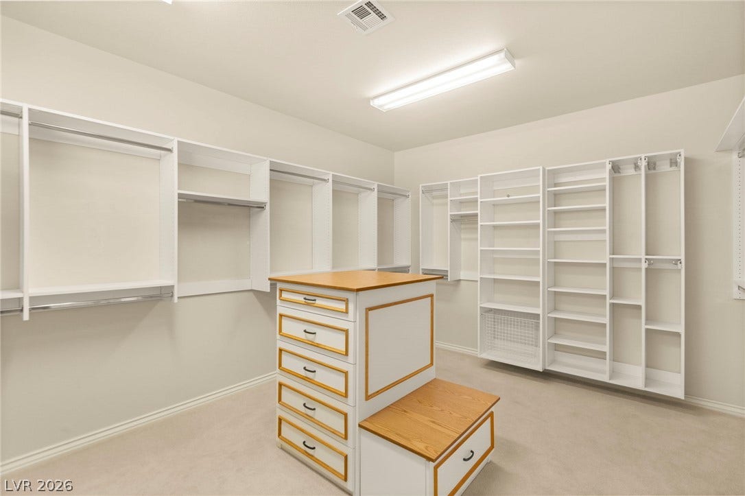 A custom organized walk-in closet boasts extensive built-in shelving, hanging rods, and a central storage island with his and hers jewelry locking drawers.