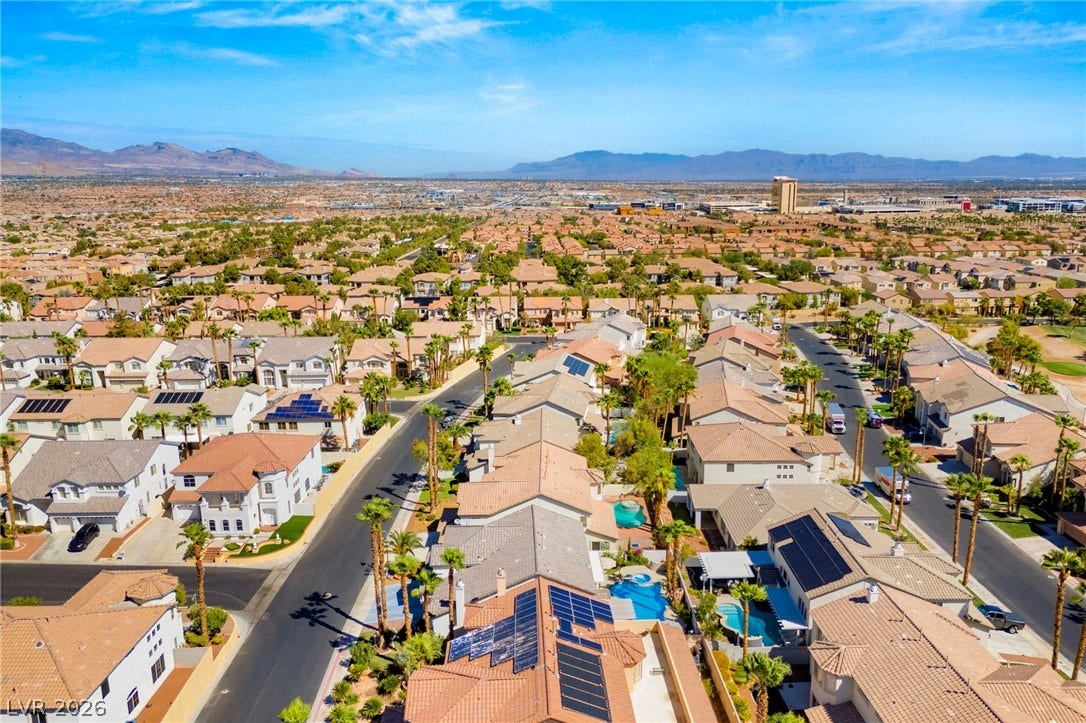 A sprawling neighborhood landscape unfolds under clear blue skies with distant mountain silhouettes.