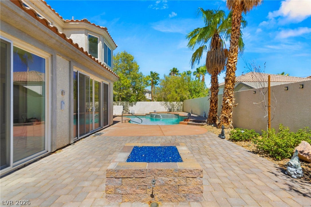 A spacious stone patio showcases a custom fire pit alongside a sparkling backyard swimming pool.