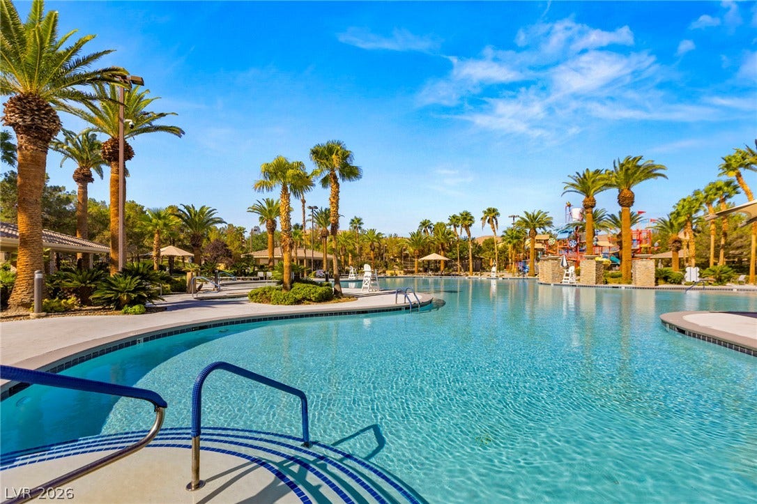 Lush palm trees line a massive resort-style swimming pool under clear blue skies.