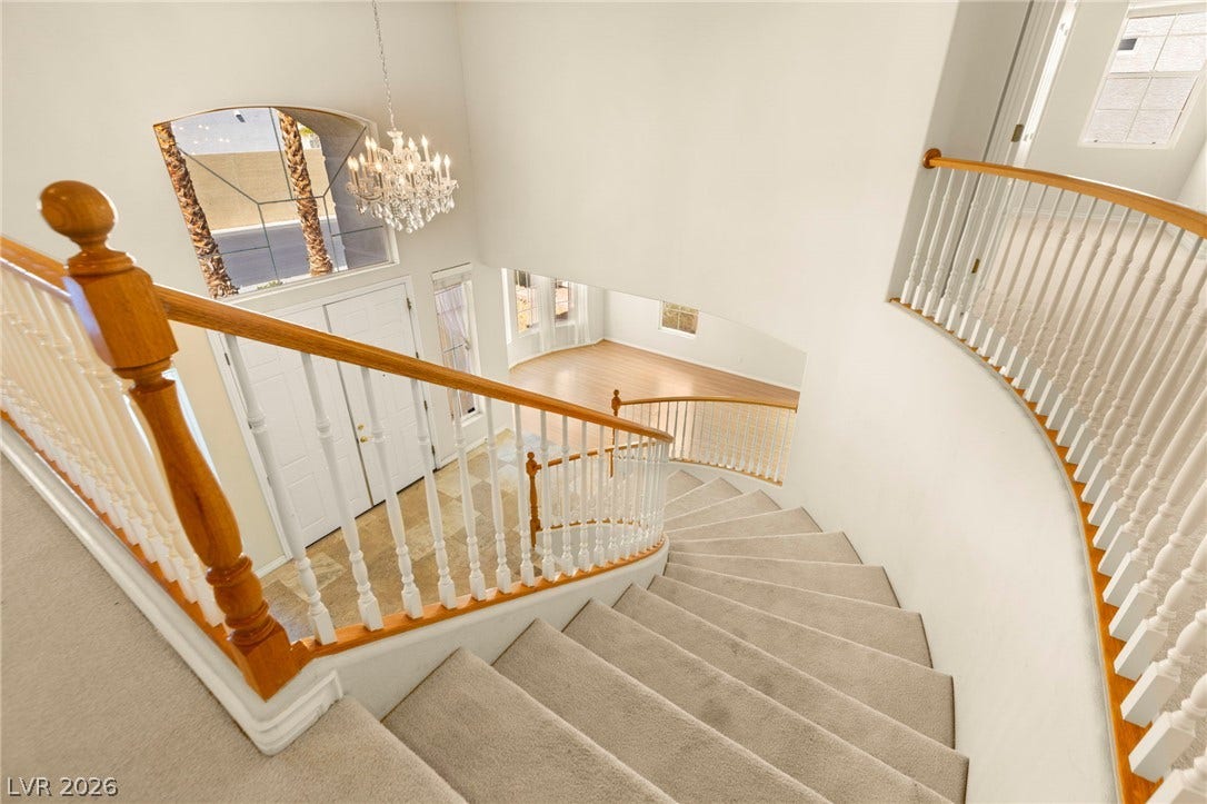 An elegant curved staircase descends into a spacious entryway highlighted by a grand chandelier.