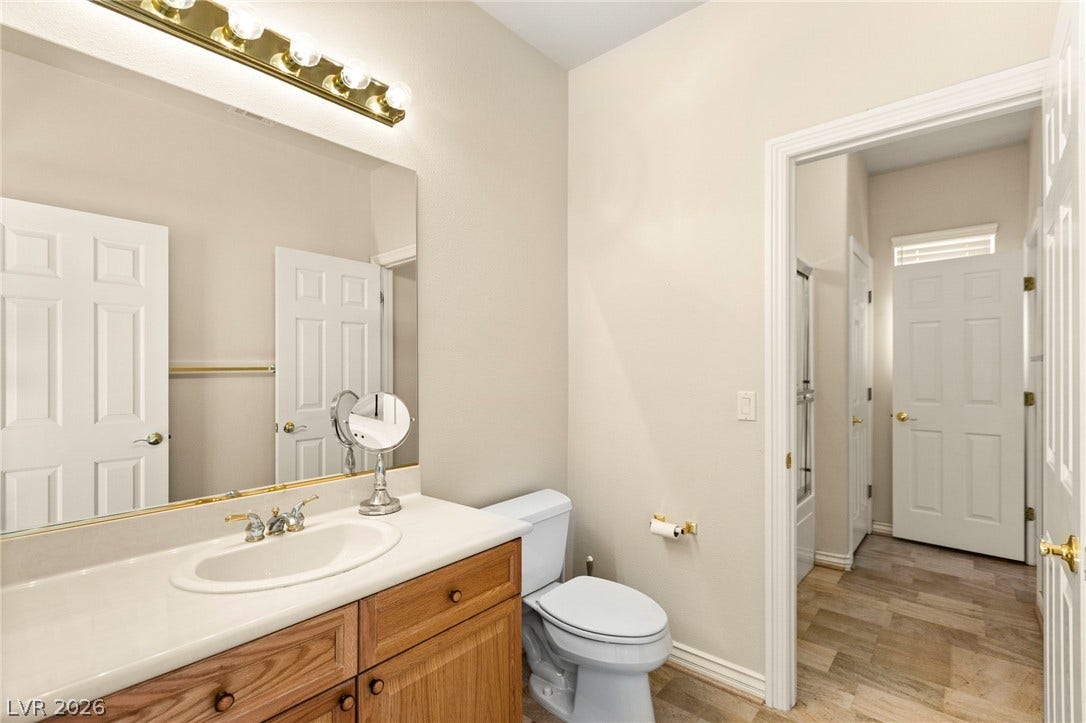 An inviting vanity area with a wooden cabinet and bright lighting guides the way inside.