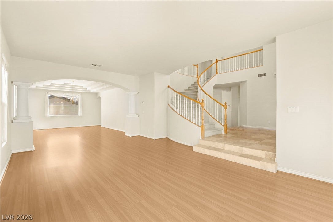 An open entryway flows into expansive living spaces under soaring ceilings with wood flooring.