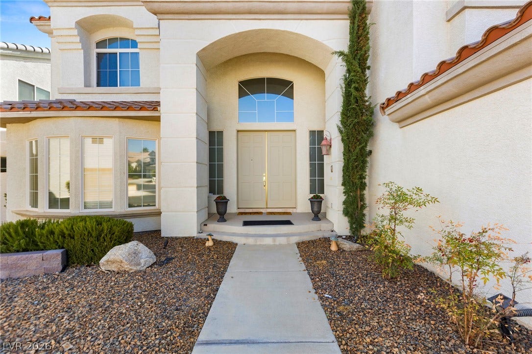 A grand arched entry porch leads to double front doors set against classic stucco architecture.