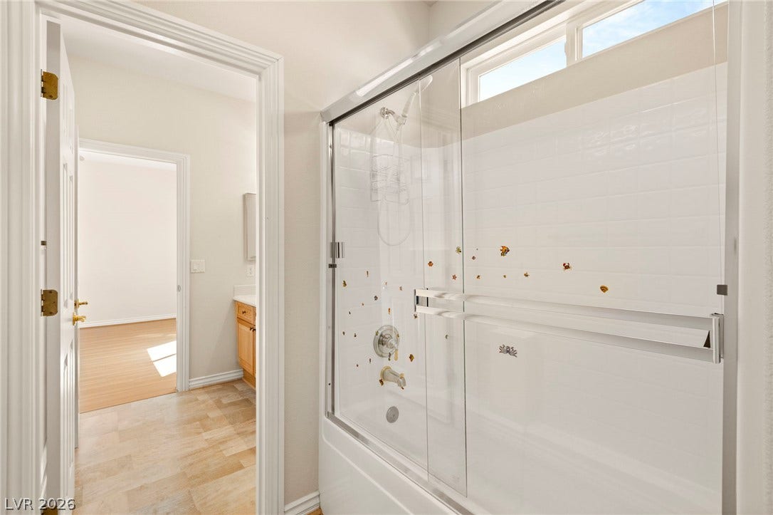 Tiled shower and tub combination sits adjacent to a bright entryway and vanity.