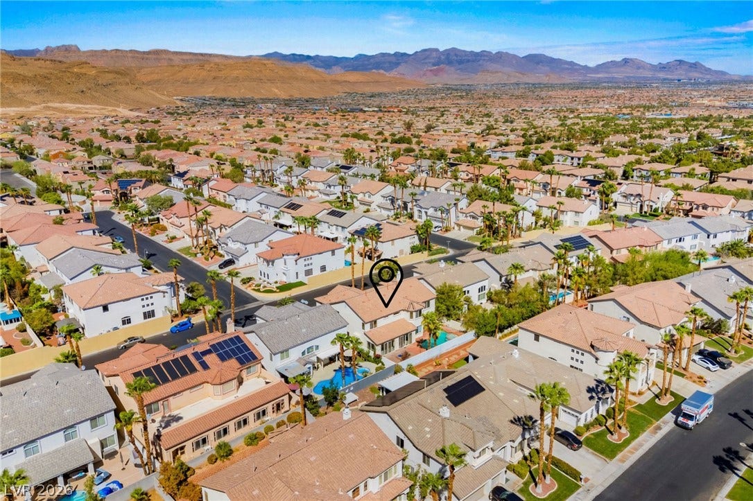 A quiet residential neighborhood of modern tile-roof homes sits framed by distant desert mountains.