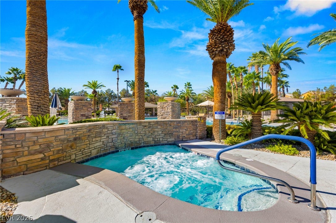 Towering palm trees and stacked stone walls surround a bubbling outdoor spa.