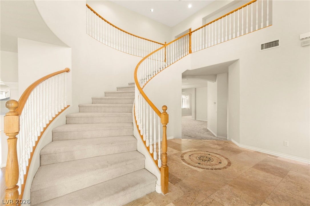 An elegant curved grand staircase anchors this grand entry featuring custom travertine flooring.