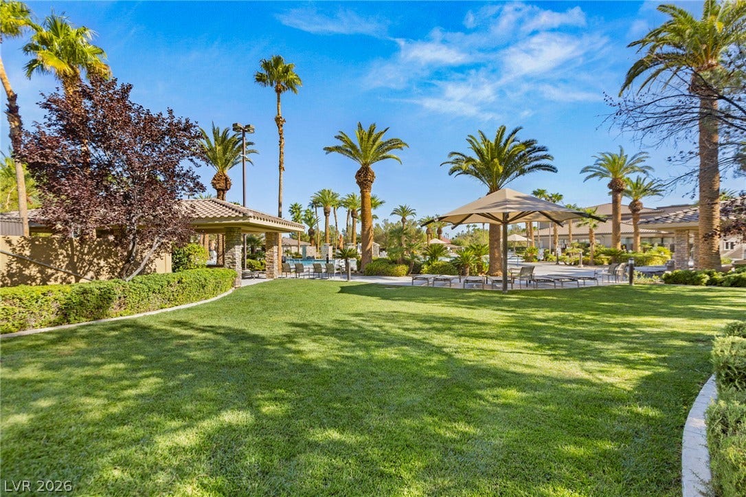 Lush green lawns and mature palm trees surround this inviting outdoor community picnic space within the enclosed community pool area.