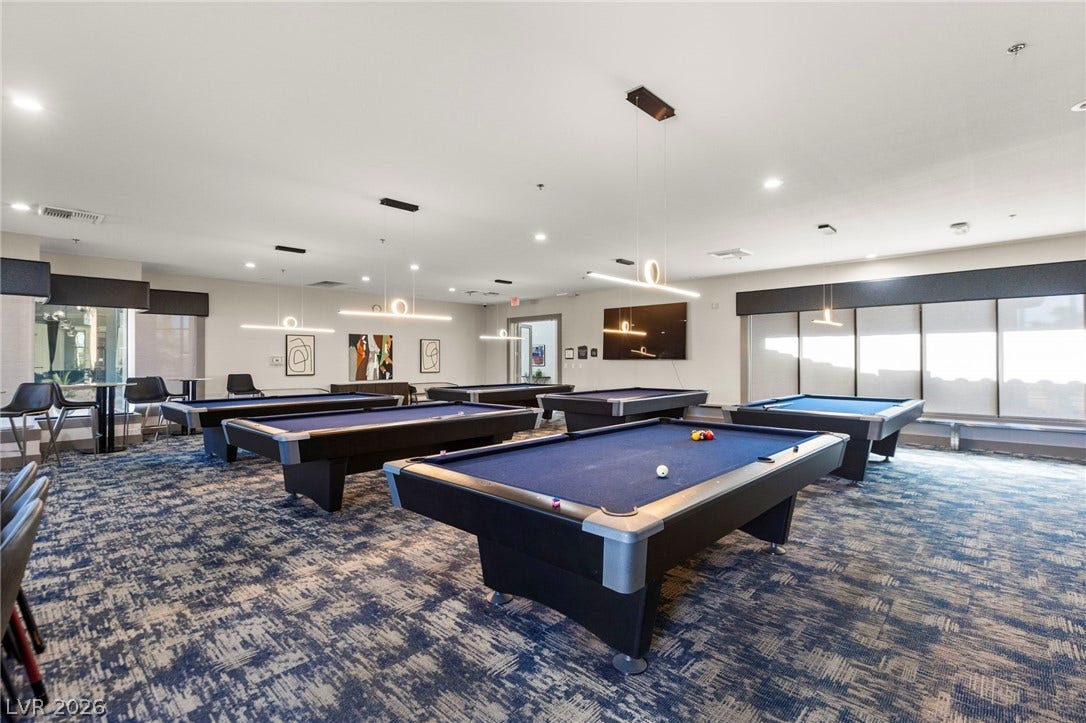 A spacious recreation room features patterned carpeting and recessed lighting above multiple billiards tables.