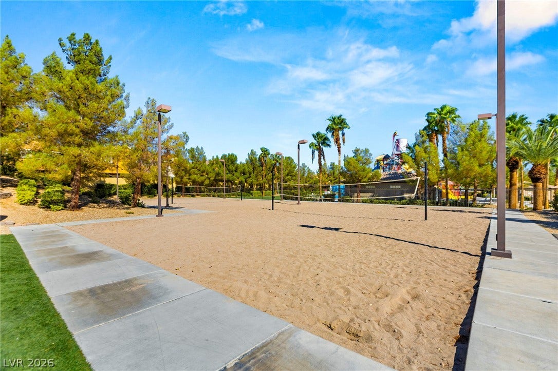 A spacious sand volleyball court is bordered by paved walkways under a clear blue sky, adjacent to rec center amenties.
