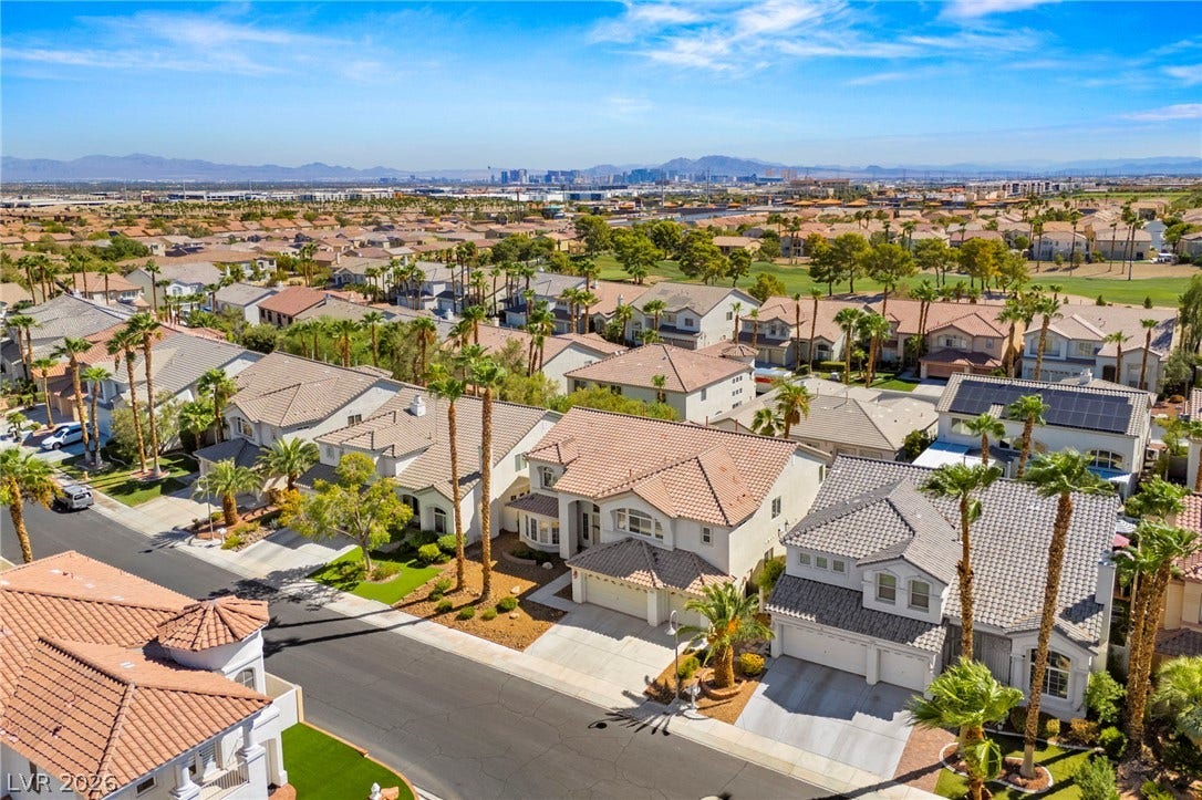 A quiet residential street winds through an established neighborhood with a distant skyline view.