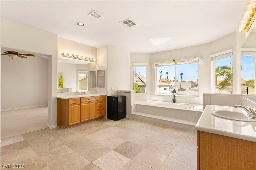 Natural light pours over the tile flooring, soaking tub, and double vanity.