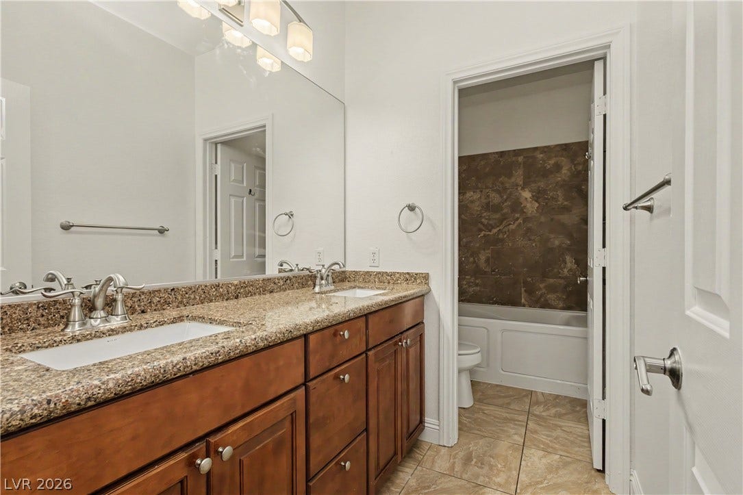 1424 Clipperton Avenue, Henderson, NV 89074 Polished stone counters and warm wood cabinetry elevate this classic primary bathroom design.