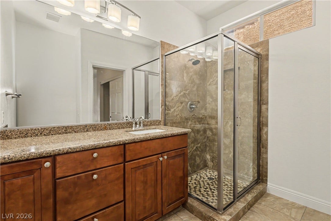 1424 Clipperton Avenue, Henderson, NV 89074 Rich wood cabinetry paired with granite countertops stands beside a glass-enclosed walk-in shower.