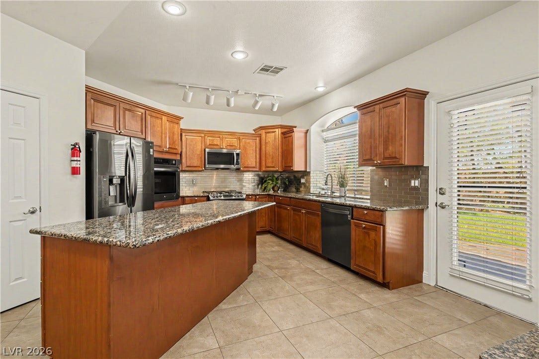 1424 Clipperton Avenue, Henderson, NV 89074 Rich wood cabinetry matches a central granite island over neutral tile flooring in this kitchen.