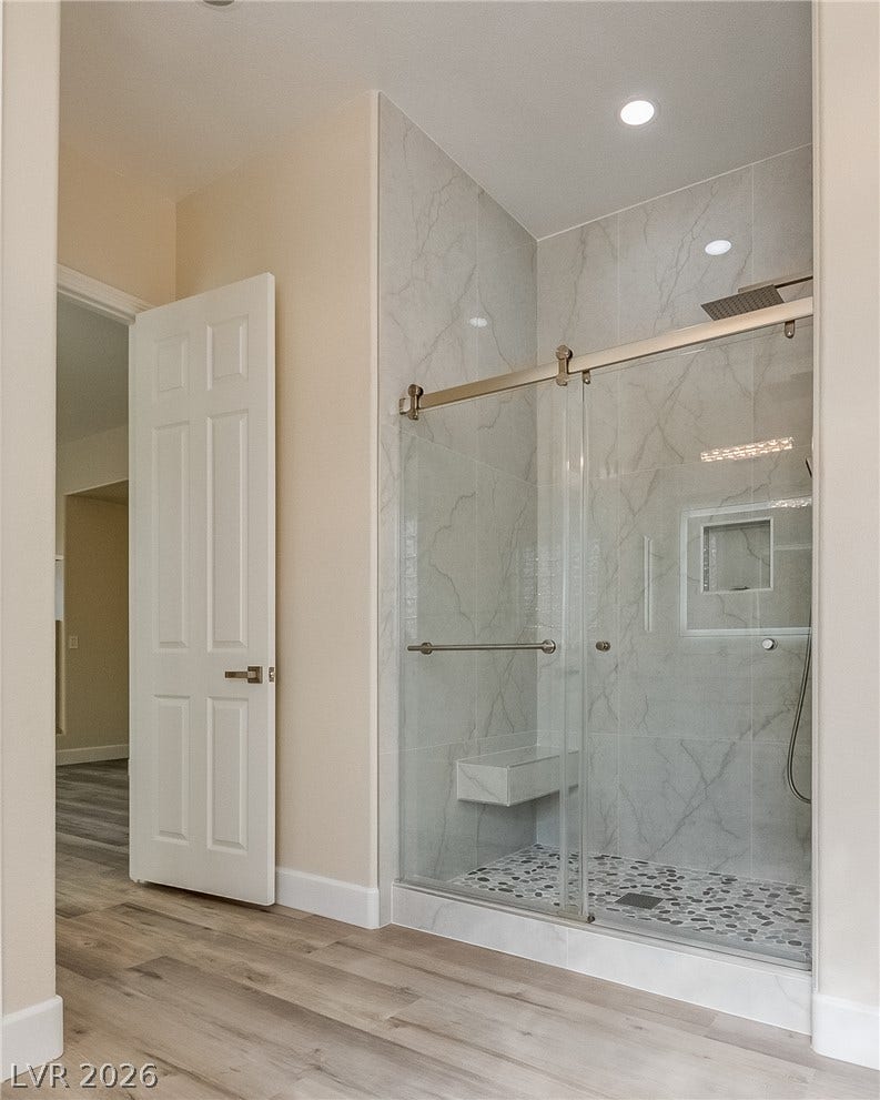 Marble-patterned tile wall surrounds a spacious walk-in shower with sliding glass doors.