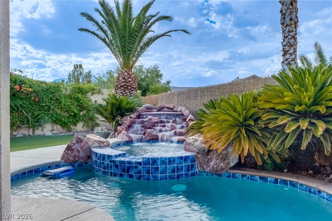 Lush tropical plantings and a rock waterfall elevate this custom backyard pool area.