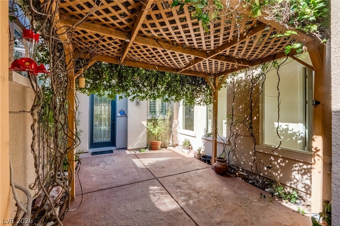 A wooden lattice pergola shades a concrete courtyard leading to the private entryway.