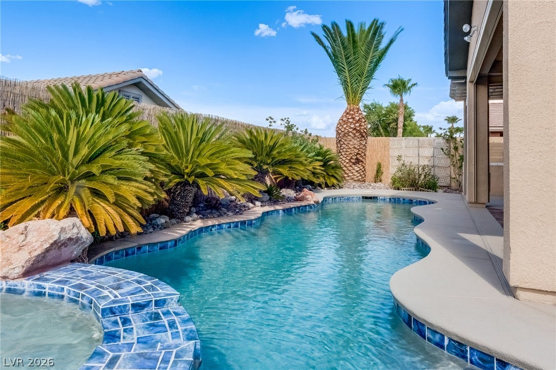 Lush palm trees line a custom curved swimming pool next to a covered patio.