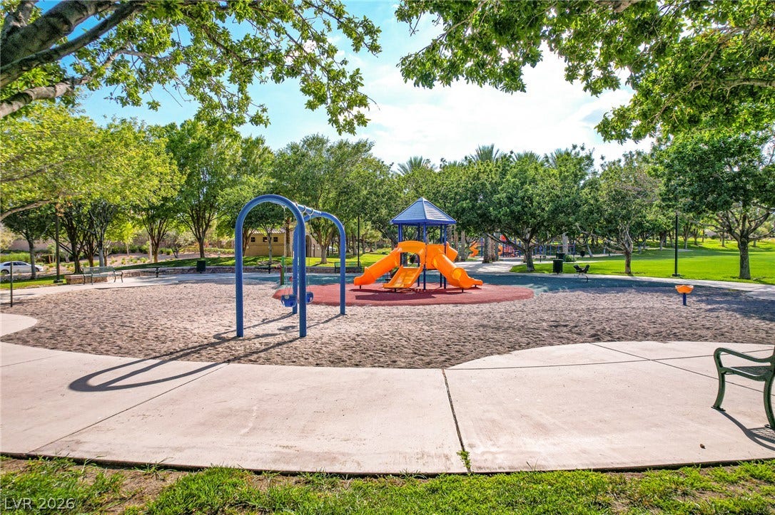 Mature trees shade a neighborhood park featuring a fully equipped play area and concrete walkways.