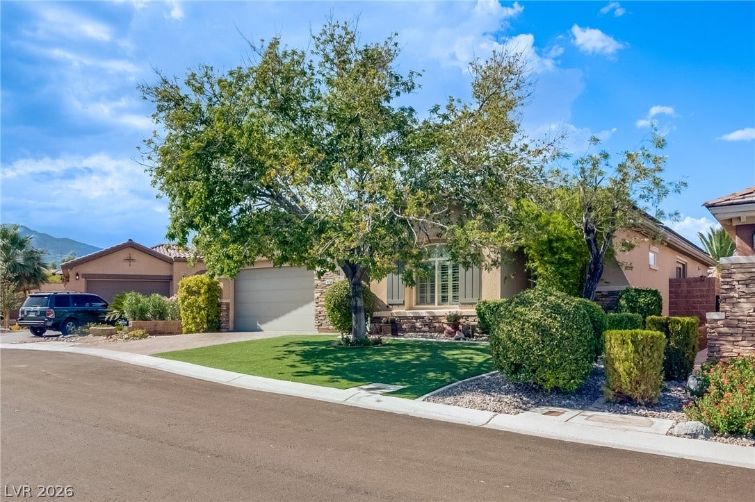 Mature trees shade the manicured front lawn of this desert-style home with stone veneer accents.