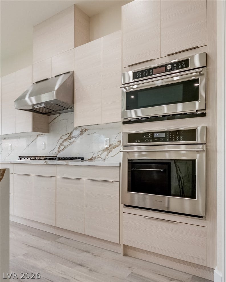 Minimalist cabinetry pairs with integrated stainless steel appliances and a bookmatched marble backsplash.
