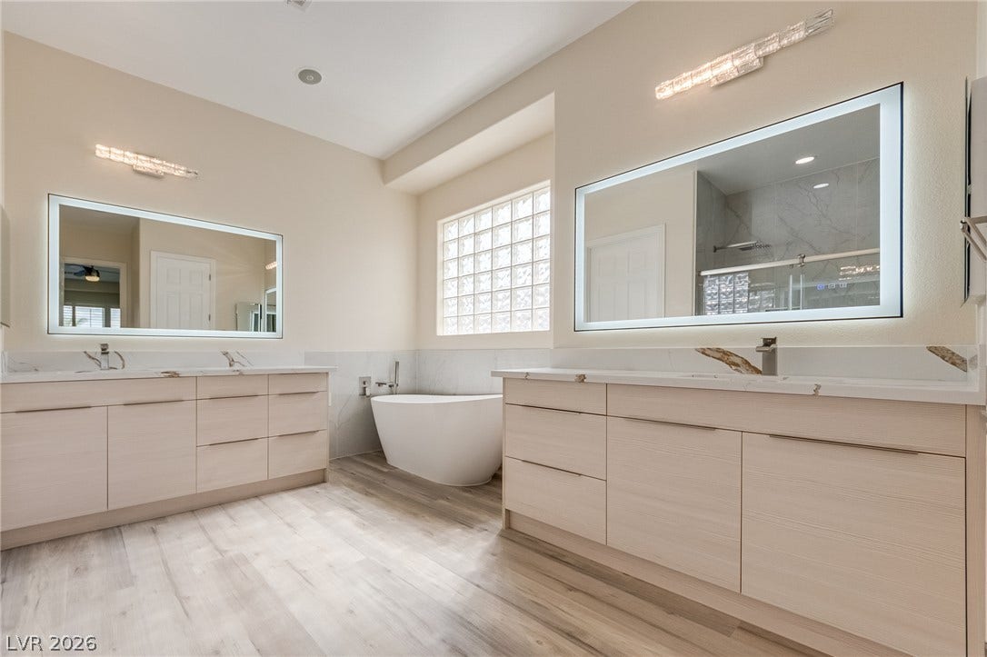 Dual vanities and a freestanding soaking tub anchor this refined bathroom with wood-look flooring.
