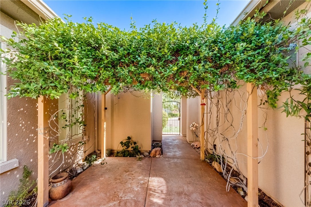 Lush climbing vines drape over a sturdy wooden arbor shading the courtyard entryway.