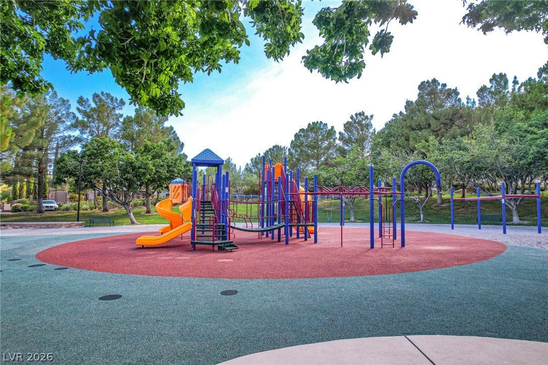 Mature trees frame a neighborhood playground with colorful climbing structures and swings.